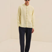 Man wearing a light yellow shirt and dark pants against a beige background